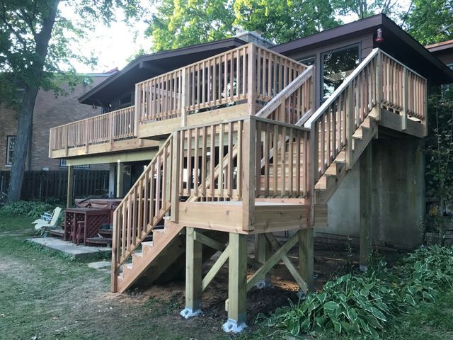 Two-level wooden deck with stairs in a backyard.