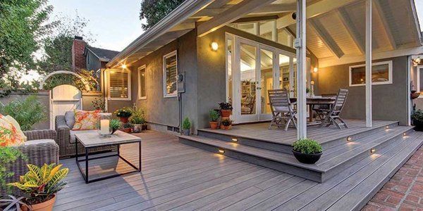 Outdoor patio with gray wooden deck, seating area, and dining table, with a house in the background.