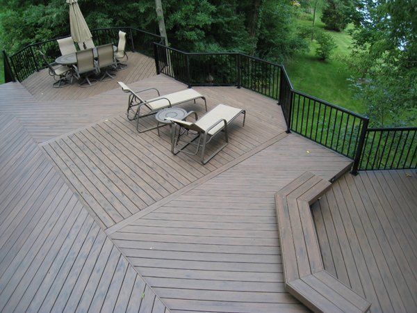 Multi-level wooden deck with seating areas, black railing, and surrounding greenery.