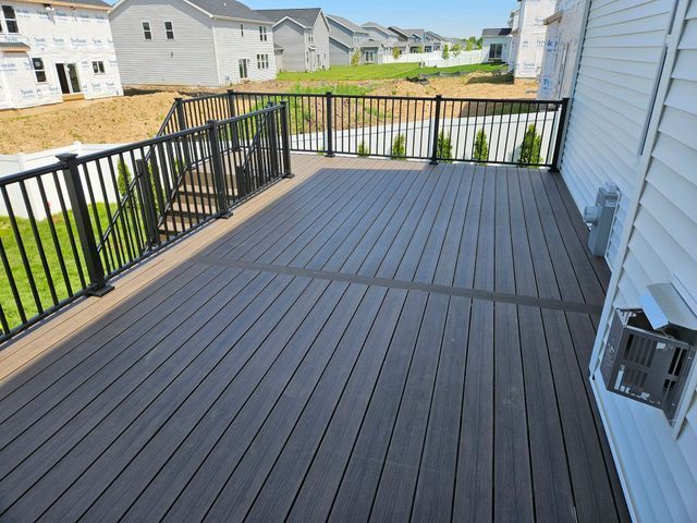 Composite deck with black railing next to a house with an air conditioner.