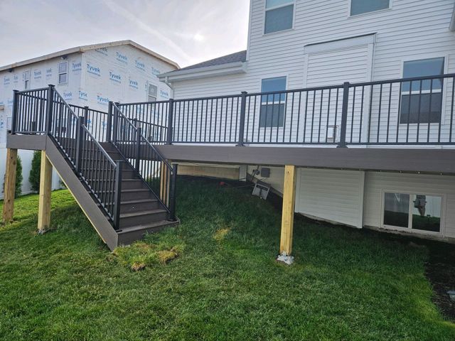 Brown deck with black railing and stairs attached to a white house, set on green grass.