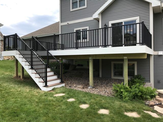 Black railed deck with stairs attached to a gray house. White trim and green grass surround it.