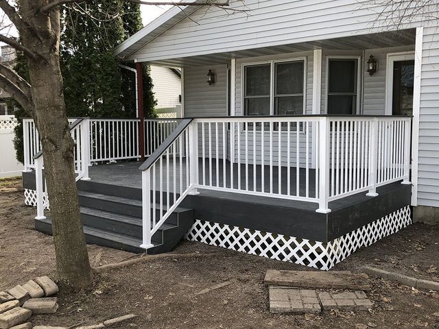 Gray and white deck with steps and railing, lattice skirting, and a tree in front of a house.