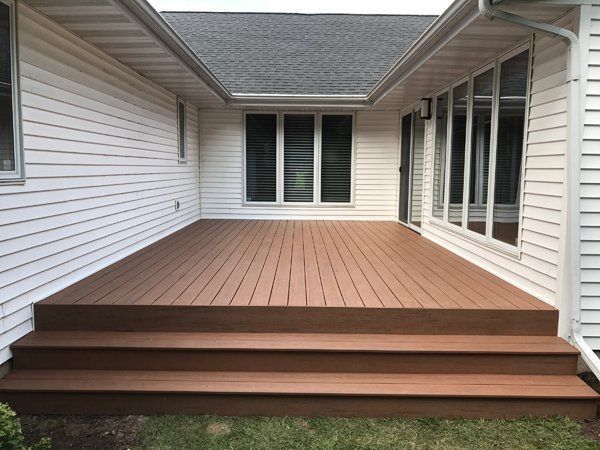 Brown composite deck with three steps, attached to a white house with windows.