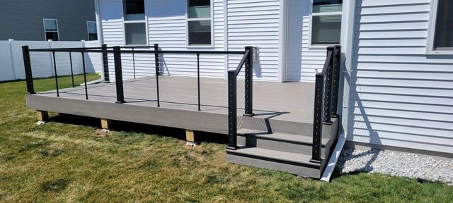 Gray deck with black railing and steps attached to a white house with windows, set in a grassy yard.