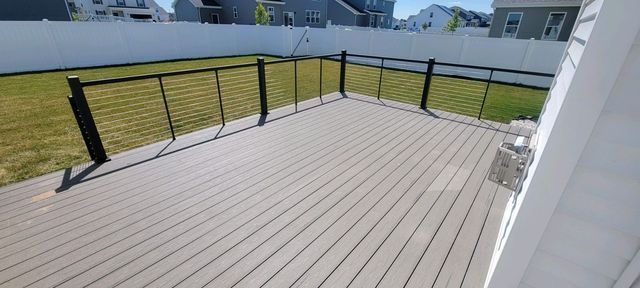 A gray wooden deck with black railings overlooks a grassy yard, enclosed by a white fence.