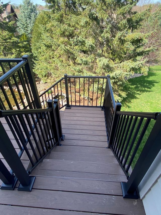 Deck stairs with black railings and brown decking, leading down to a grassy yard.