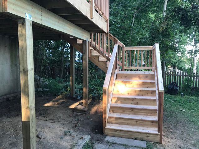 Wooden deck with stairs leading down to a yard; the stairs have railings and the deck is supported by wooden posts.