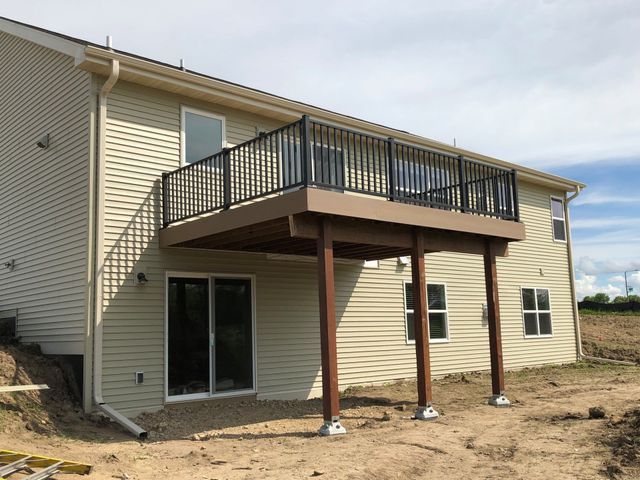 Tan house with brown deck, black railings, supported by brown posts on concrete bases.