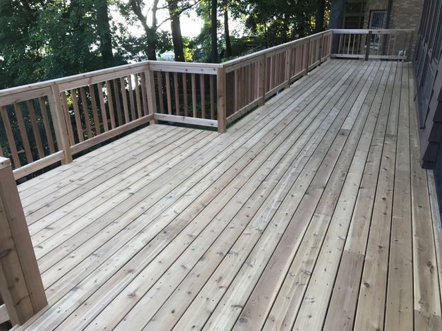 Wooden deck with railings, set outdoors among trees.