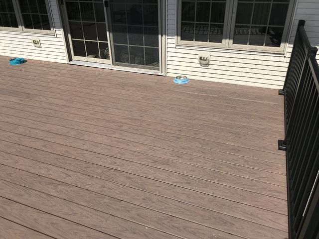Brown composite deck with black railing against a white house with sliding glass door and windows.