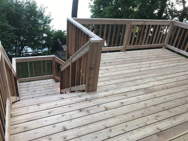 Wooden deck with stairs, railing, and view of trees.