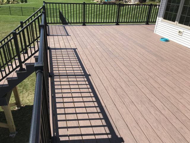 Brown composite deck with black railings and steps, overlooking a green lawn.