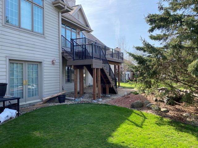Backyard view: a two-level deck with stairs, a house with light siding, and green grass.