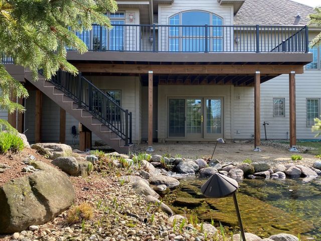A two-story deck with black railings and stairs overlooks a small pond with rocks.