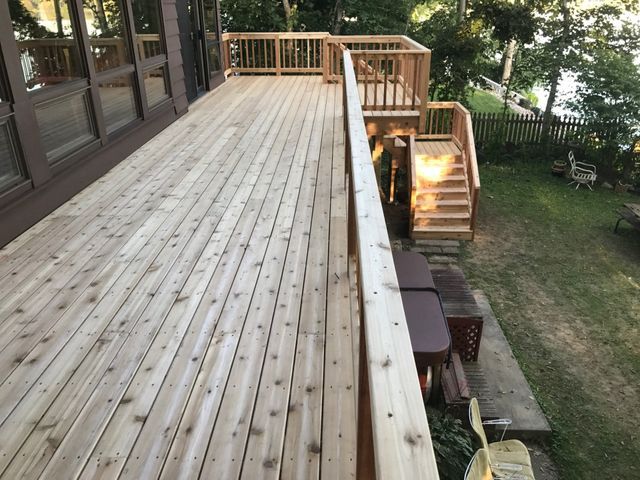 Wooden deck with stairs leading to a lower level, overlooking a body of water with trees.