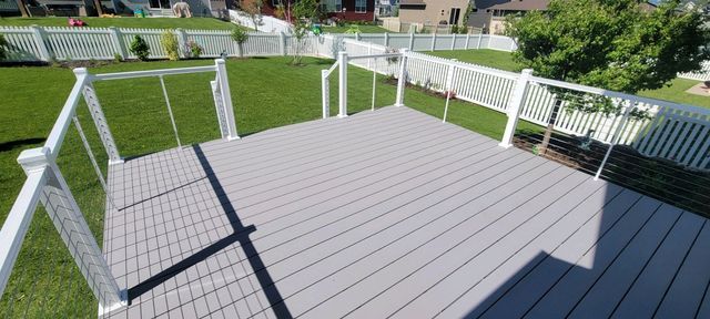 Elevated gray deck with white railings overlooks a green lawn and white picket fence.
