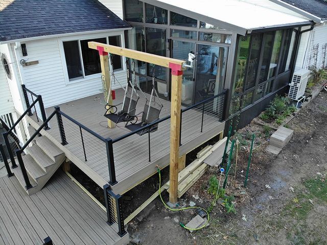 Wooden deck with swing set, black railing, and screened sunroom.