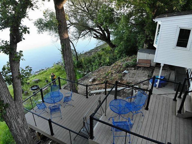 Wooden decks with blue patio furniture overlooking a river. A white building is visible on the right.