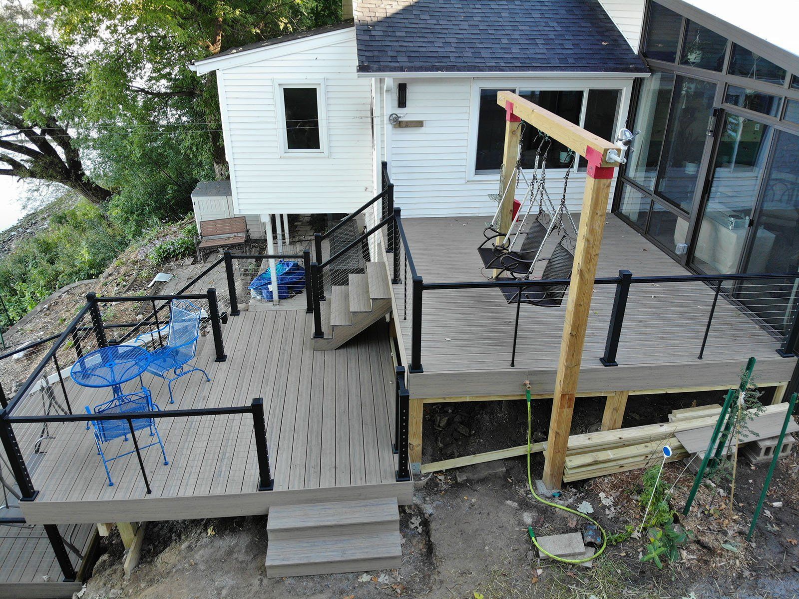 Wooden deck with black railings and swing set next to a white house overlooking a body of water.