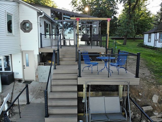 Multi-level deck with black railings and cable, leading to a house, swing, and outdoor seating.