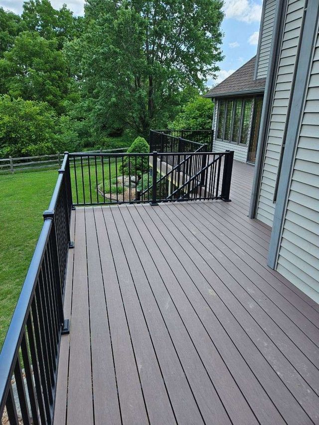 Brown composite deck with black railing overlooking a green lawn and trees.