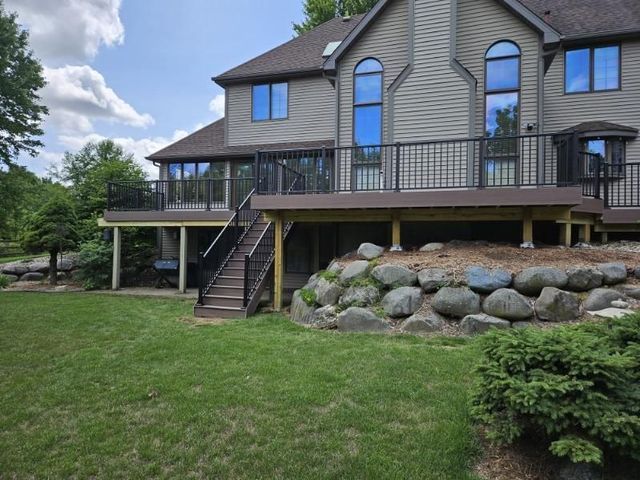 Two-story house with a wooden deck, a rock wall, and green lawn.
