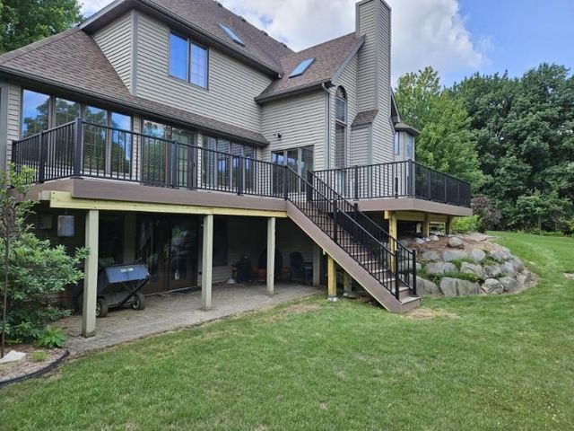 A two-story house with a deck and stairs overlooking a grassy backyard.