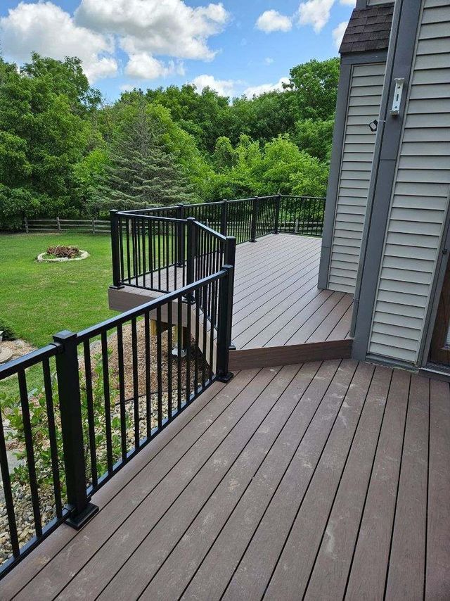 A deck with dark gray railings and brown composite decking, overlooking a green lawn and trees under a blue sky.