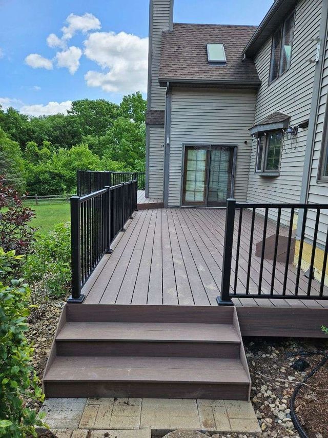Wooden deck with black railings and steps leading to a house with a gray exterior.
