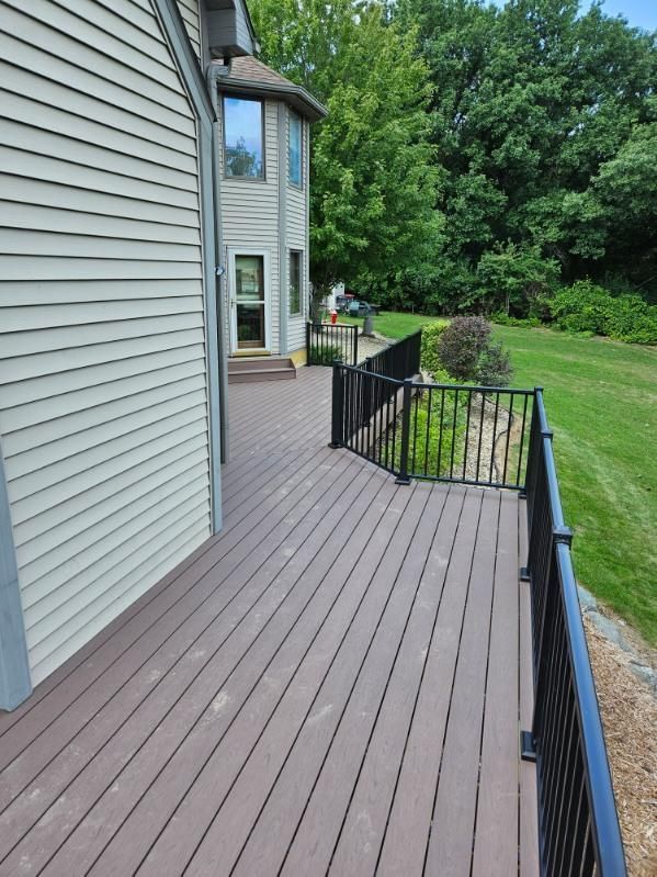 Brown composite deck with black railing next to a house with light green siding and a grassy yard.
