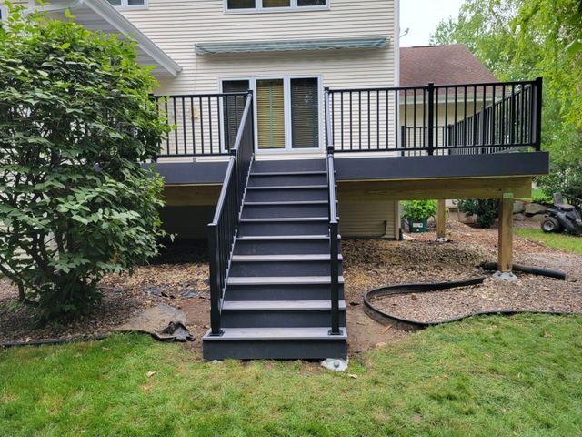 Deck with black railings, stairs, and gray decking, leading to a house with sliding glass doors.
