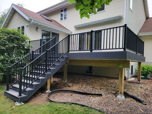 Black railing deck with stairs attached to a beige house, set in a yard.