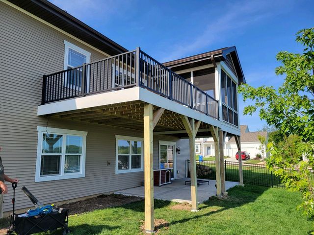 Two-story home with a deck and screened-in porch, black railing, light-colored posts, and a blue sky.