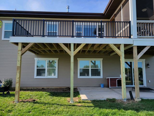 A raised deck with black railing and light brown siding, supported by wooden posts.