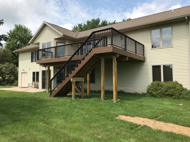 Two-story house with a wooden deck and black railing, connected by stairs.