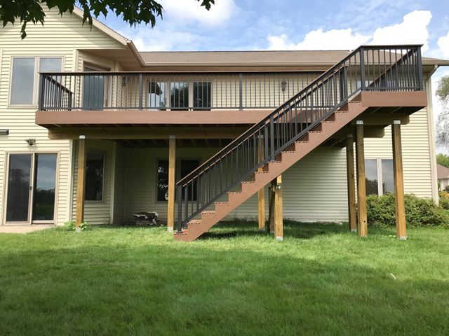 Beige house with a brown deck and black railings, accessible via stairs.