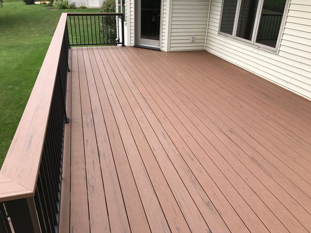 Brown composite deck with black railing next to a house with beige siding and a glass door.
