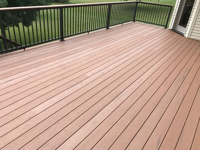 Brown composite deck with black railing overlooking a green lawn.