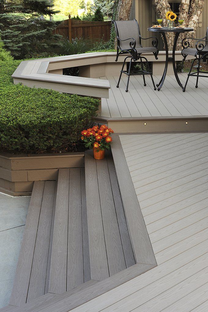 Gray composite deck with steps, a small table, chairs, and potted flowers.