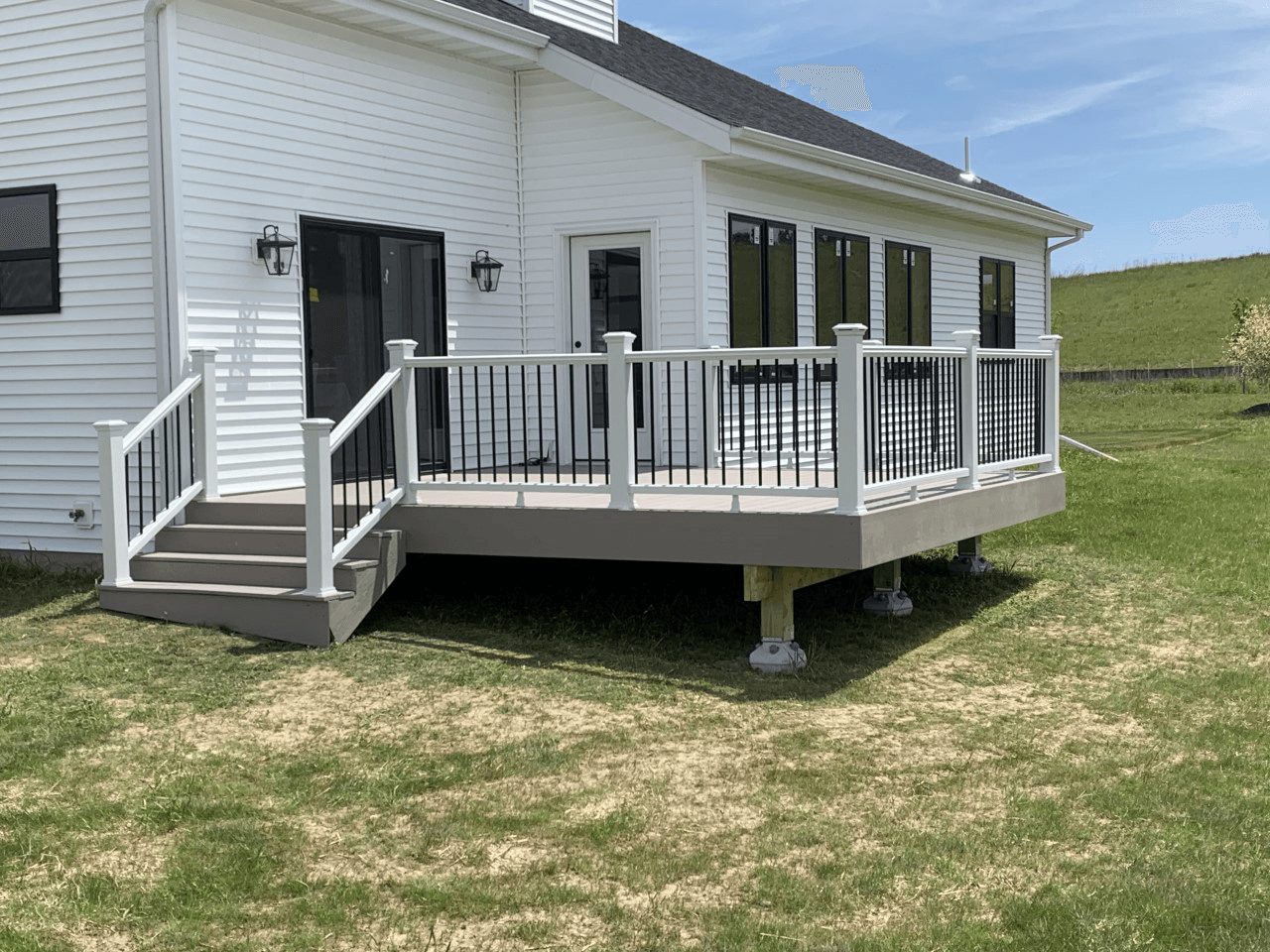 A white house with a gray deck. The deck has white railings and stairs, with a black door and windows.