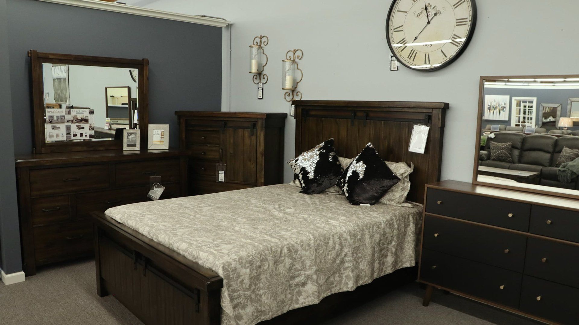 A bedroom with a bed, dresser, mirror and clock on the wall.