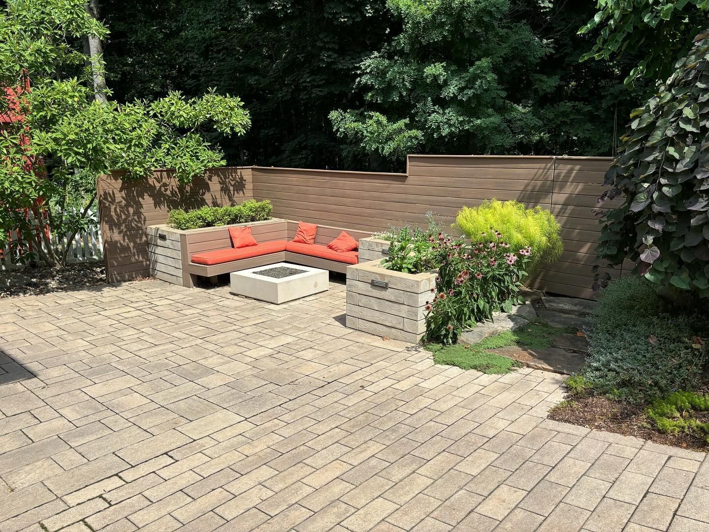 Patio with brick pavers, sectional seating with orange cushions, fire pit, and planters.