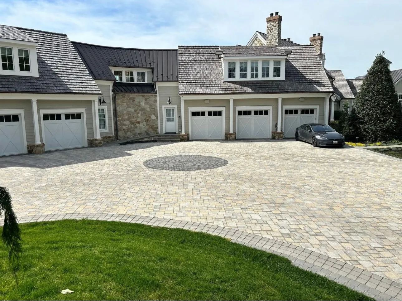 Exterior view of a house with a stone and gray facade, a multi-car garage, and a brick driveway.