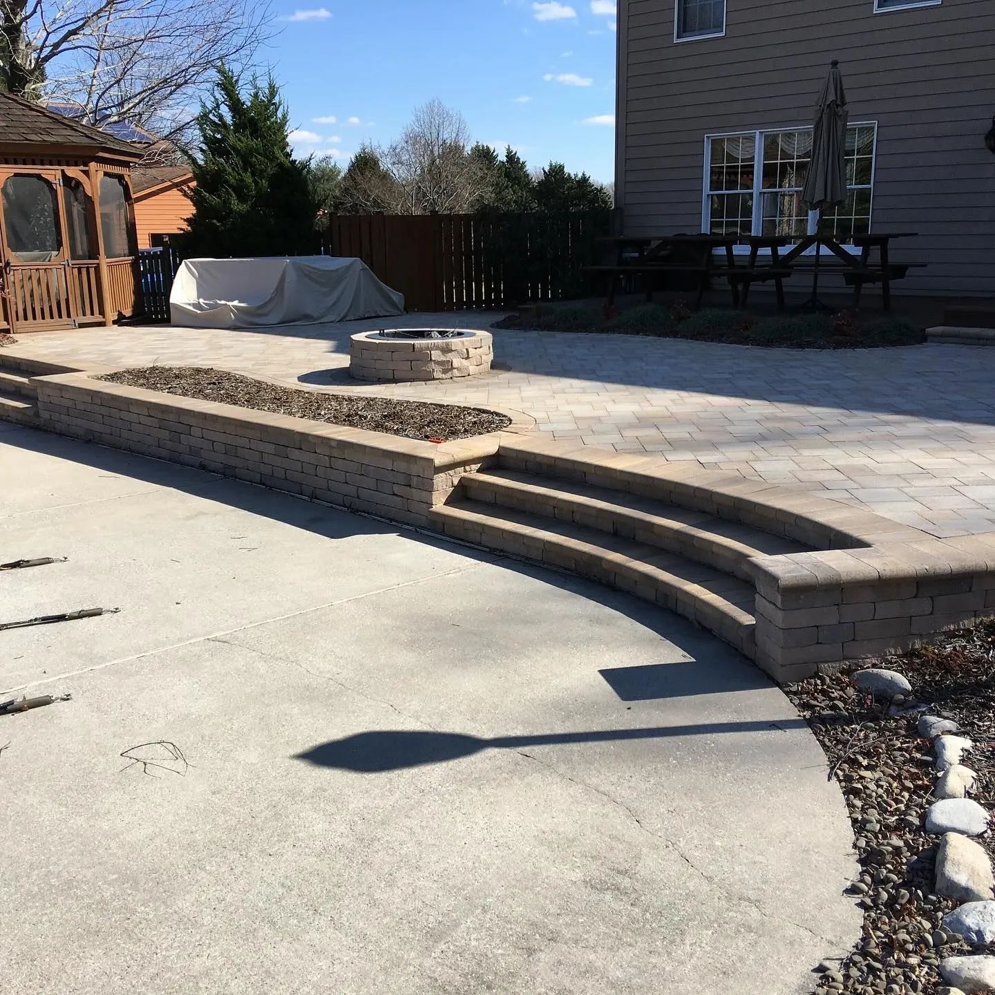 Patio with curved steps, fire pit, and retaining wall. Gazebo and house in the background.