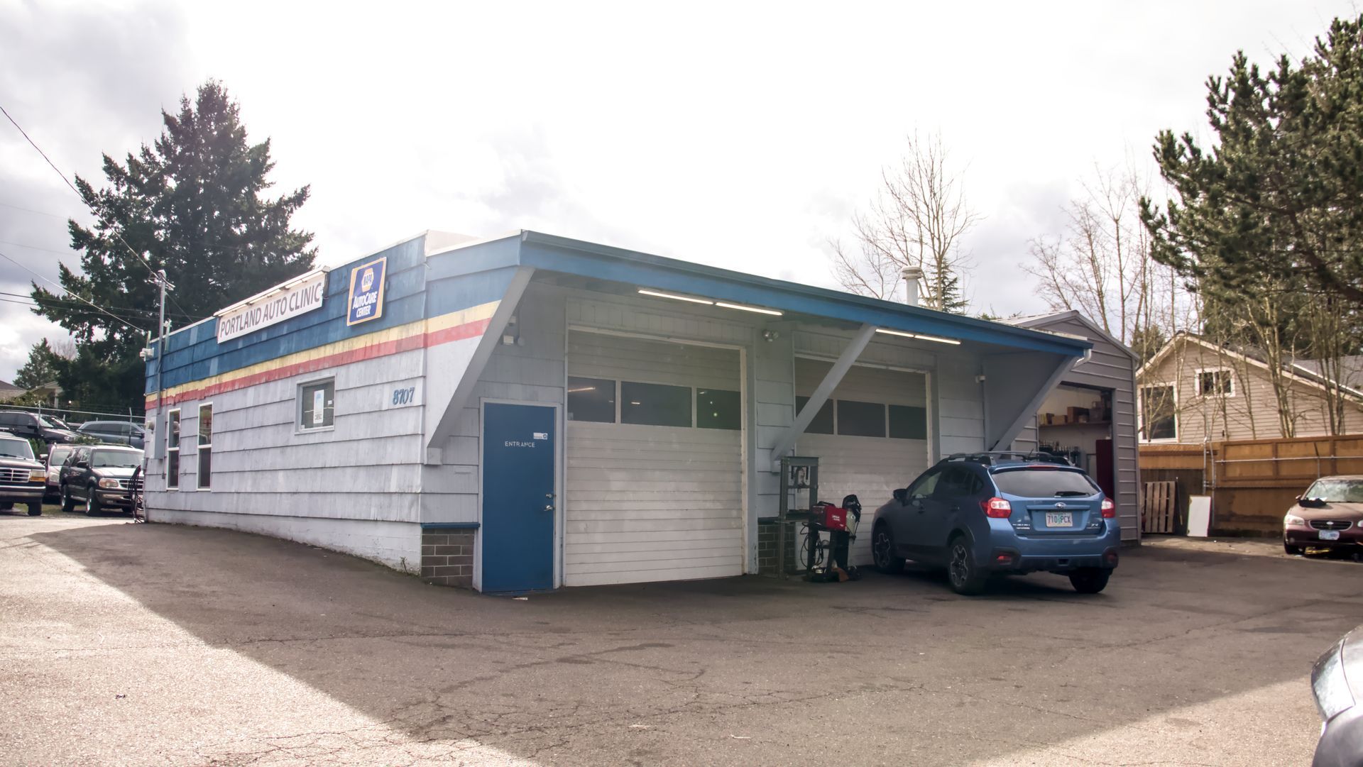 Auto repair shop with blue and white facade; car parked in front of open garage door.