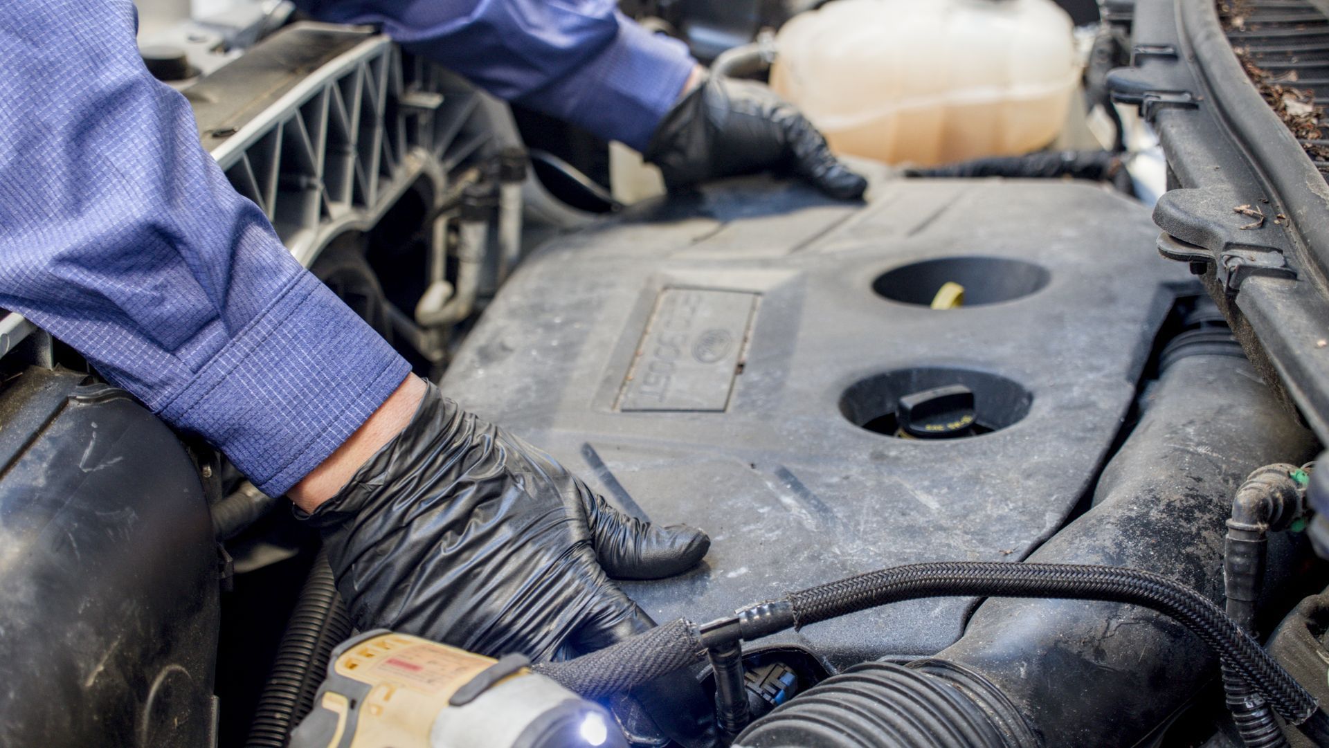 Mechanic working on car engine, wearing gloves.