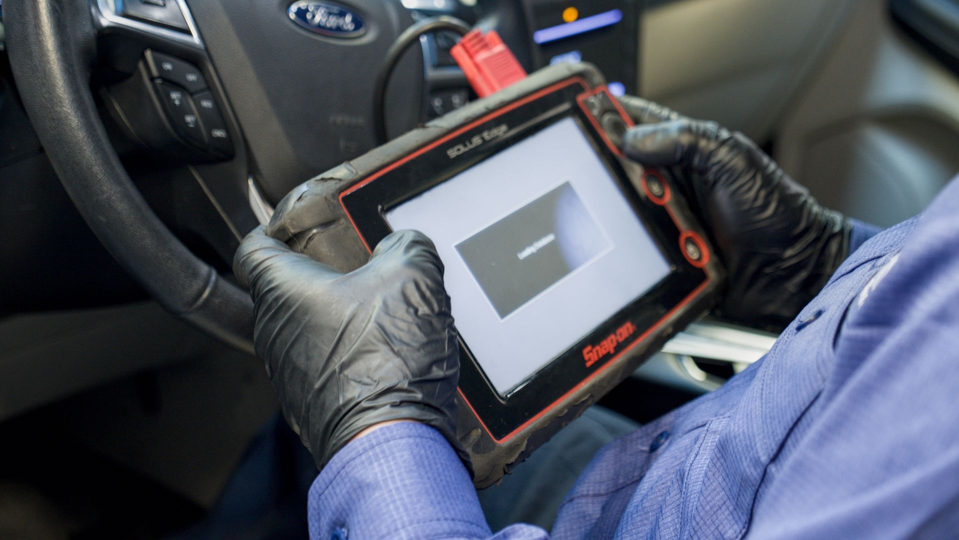 Person in black gloves using a Snap-on diagnostic tool in a car.