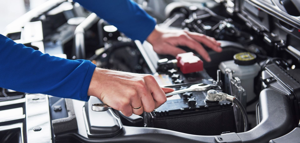 A person working on a car engine, using a wrench.
