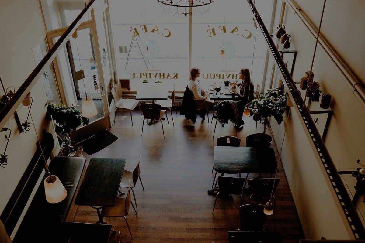 Cozy loft cafe with wooden floors, string lights, and a few people seated at tables near large windows.